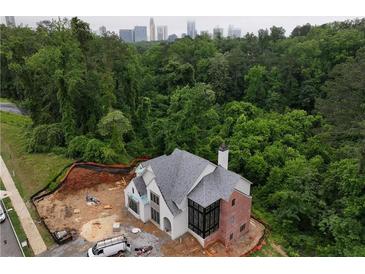 New construction home with gray roof and brick accents surrounded by lush green trees and a city skyline in the background at 469 Emily Reed Lot 11 Ln, Atlanta, GA 30342