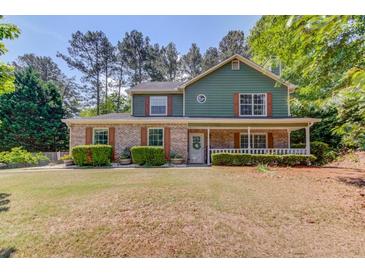 Charming two-story home featuring a brick facade, green siding, a covered front porch, and a well-manicured lawn at 3987 Ivory Gables Pl, Buford, GA 30519