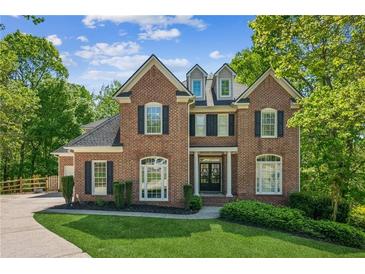 Elegant two-story brick home featuring dormer windows, a manicured lawn, and lush landscaping at 4750 Spring Wood Trce, Cumming, GA 30041