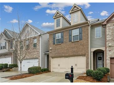 Charming townhome featuring a two-car garage and brick facade, complemented by manicured landscaping at 6595 Story Cir, Norcross, GA 30093