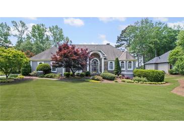 Charming home featuring a large front lawn with mature landscaping, trees, and architectural roofline at 6725 Polo Dr, Cumming, GA 30040