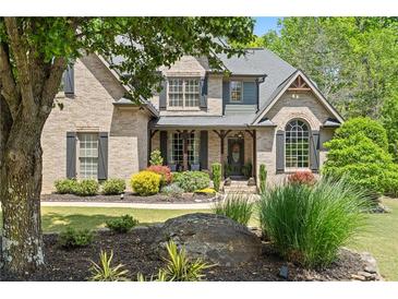 Charming brick home featuring a beautifully landscaped front yard with mature trees and colorful flower beds at 5885 Wild Azalea Cv, Sugar Hill, GA 30518