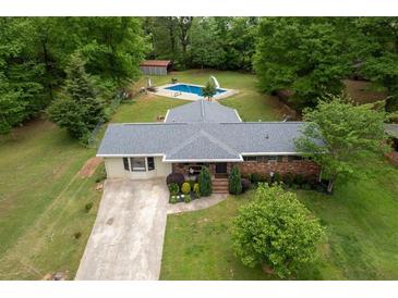 An aerial view shows home with pool and shed surrounded by mature trees in a large green yard and long driveway at 3833 Coral Ln, Douglasville, GA 30135