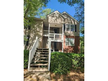 Two-story condo featuring brick accents, wood siding, a front porch, and staircase entrance surrounded by lush landscaping at 446 Teal Ct, Roswell, GA 30076