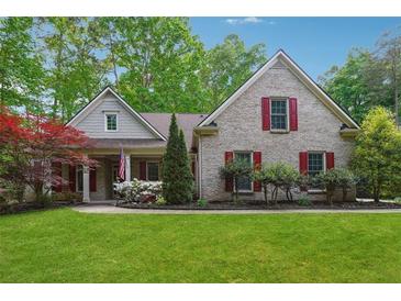 Charming, light brick home featuring well-manicured lawn, red shutters, and lush landscaping at 7045 W Mountain Xing, Cumming, GA 30041