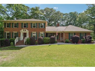 Charming two-story brick home with a well-manicured lawn, mature trees, and traditional design elements at 5027 Castlewood Sw Dr, Lilburn, GA 30047