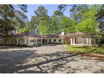 Mediterranean-style home with brick driveway, multiple garages, and covered porch, framed by mature trees at 9355 Huntcliff Trce, Sandy Springs, GA 30350