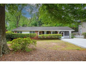 Charming brick home with a covered porch and landscaped front yard featuring mature trees and manicured bushes at 3501 Montreal Way, Tucker, GA 30084