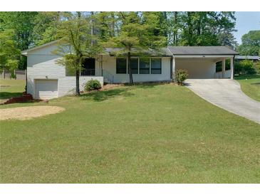 Charming white brick home with a well-maintained lawn and a long driveway leading to a carport at 1987 Darrell Dr, Marietta, GA 30066