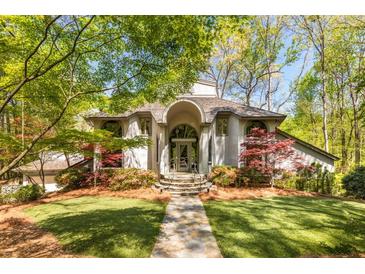 Stunning home exterior with an arched entryway, stone path, lush lawn, and colorful landscaping surrounded by mature trees at 6525 Old Riverside Nw Dr, Sandy Springs, GA 30328