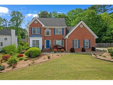 Charming red brick two-story home with manicured lawn and blue shutters and a blue front door at 1665 Little Lisa Ln, Snellville, GA 30078