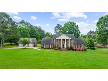 Brick home featuring a lush green lawn, tall white columns, black shutters, and a detached garage at 130 Plantation Dr, Stockbridge, GA 30281