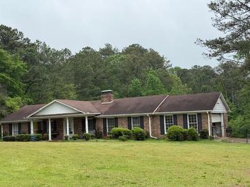 Charming single-story brick home with a cozy front porch and a lush green lawn surrounded by trees at 1935 Flat Shoals Se Rd, Conyers, GA 30013