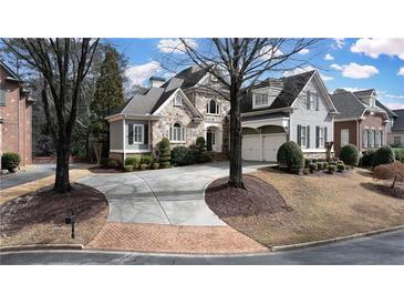 Charming home with stone facade, gray siding, well-manicured lawn, and curved driveway leading to attached garage at 185 Windsor Cv, Sandy Springs, GA 30328