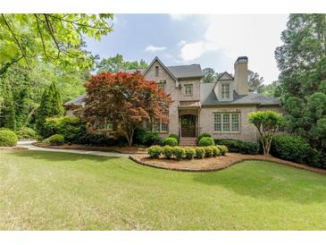 Charming brick home featuring a manicured lawn, mature trees, and classic architectural details at 1575 Spalding Dr, Sandy Springs, GA 30350