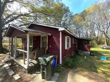Exterior of a red single-story home with a covered front porch and overgrown yard at 6475 Church St, Atlanta, GA 30291