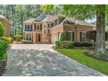 Elegant two-story home with brick and stone facade, complemented by a lush green lawn and mature trees at 5303 Davenport Mnr, Cumming, GA 30041