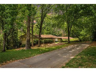 Charming single-story home with lush landscaping and a long driveway, nestled among mature trees at 12080 Mountain Laurel Dr, Roswell, GA 30075