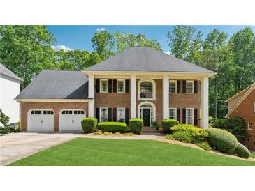 Stately brick home featuring a three-car garage and a beautifully manicured lawn with lush landscaping at 320 Rossiter Rdg, Alpharetta, GA 30022