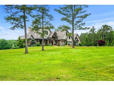 Sprawling lawn and mature trees frame this charming, stone-accented, two-story home under a bright blue sky at 1101 N Flat Rock Rd, Douglasville, GA 30134