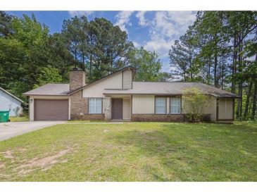 Traditional-style home featuring mature trees, a driveway, attached garage, and well-maintained lawn at 1774 Northwick Pl, Lithonia, GA 30058