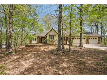 Charming home exterior with light yellow siding, brick accents, and a two-car garage nestled among mature trees at 33 Fawn Lake Trl, White, GA 30184