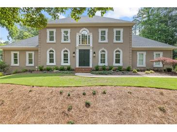 Elegant two-story home featuring a neutral facade, complemented by symmetrical windows and lush landscaping at 9950 Farmbrook Ln, Johns Creek, GA 30022