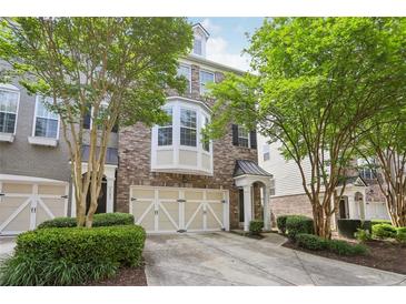 Brick townhome featuring a two-car garage and a charming covered entrance, complemented by mature trees and manicured landscaping at 6080 Indian Wood Se Cir, Mableton, GA 30126