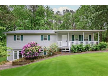 A well-maintained home featuring a green lawn, mature trees, blooming bushes, and a covered front porch at 4855 Brownsville Rd, Powder Springs, GA 30127