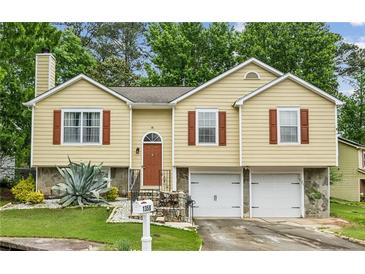 Charming yellow split-level home features brown shutters, attached two-car garage and manicured lawn at 1358 Stoneleigh Way, Stone Mountain, GA 30088