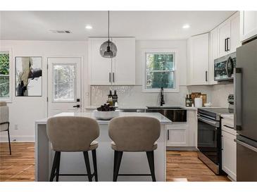 Bright kitchen features white cabinetry, stainless appliances, island with counter seating, and stylish pendant lighting at 904 Fairburn Nw Pl, Atlanta, GA 30331