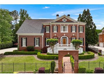 Stunning two-story brick home featuring a manicured lawn and an inviting arched entryway with black metal gate at 5070 Riverlake Dr, Peachtree Corners, GA 30097