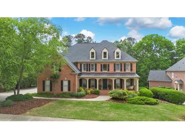 Stately brick home featuring a welcoming front porch and professionally landscaped yard with mature trees at 120 Burford Holw, Alpharetta, GA 30022