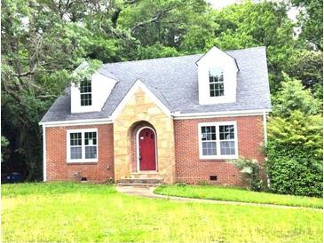 Charming red brick home featuring a stone archway, red door, dormer windows and a well-manicured lawn at 1001 Jefferson Ave, Atlanta, GA 30344
