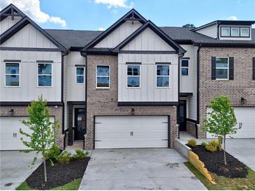 Modern townhome showcasing a two-car garage, gray brick, white siding, and black trim against a blue sky at 5706 Urban Village Way # 4, Tucker, GA 30084