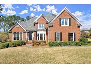 Charming brick home with a manicured front lawn, mature landscaping and black shutters on the windows at 13090 Magnolia Crescent Dr, Roswell, GA 30075