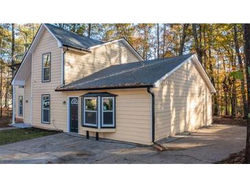 Two-story home with a driveway, tan siding and black trim and windows surrounded by trees at 7156 Whitfield Dr, Riverdale, GA 30296