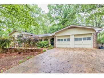 Charming home featuring an attached two-car garage and lush landscaping, set back from a long driveway, surrounded by mature trees at 2288 Hudson Sw Dr, Lilburn, GA 30047