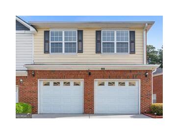 Two-story home with a double garage, brick facade, yellow siding and black shuttered windows at 988 Treymont Way, Lawrenceville, GA 30045