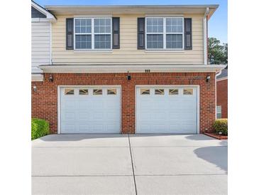 Front exterior view of a home showcasing a brick facade and a two-car garage with white doors at 988 Treymont Way, Lawrenceville, GA 30045
