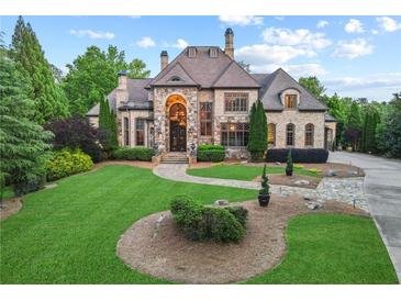 Beautiful stone home with manicured lawn and lush landscaping on a sunny day at 878 Middle Fork Trl, Suwanee, GA 30024