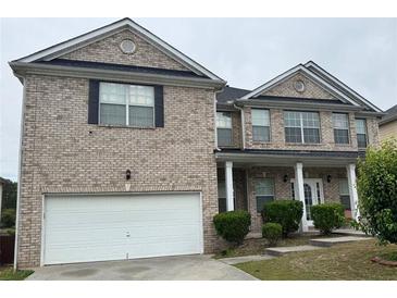 Two-story brick home featuring a two-car garage, covered front porch, and neatly trimmed landscaping at 7328 Vigo Dr, Lithonia, GA 30058