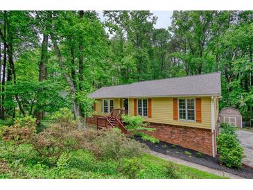 Charming exterior of a yellow home with brown shutters surrounded by lush greenery and trees at 3311 Creek Hollow Dr, Marietta, GA 30062