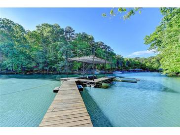 Lake view of a wooden dock with a covered sundeck in a wooded area under a bright blue sky at 975 Timber Lake Trl, Cumming, GA 30041