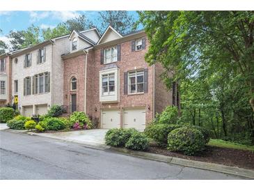 Beautiful brick townhome featuring a two-car garage and lush landscaping, enhancing its curb appeal at 7249 Village Creek Trce, Atlanta, GA 30328