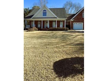 Charming brick home with a welcoming front porch, two-car garage and a large yard on a sunny day at 216 Brackin Trce, Grayson, GA 30017