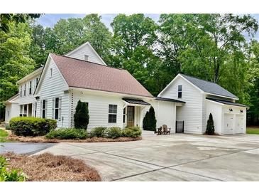 Charming white home with a spacious driveway and a detached garage, surrounded by lush greenery and mature trees at 400 N Peachtree Pkwy, Peachtree City, GA 30269