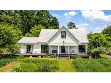 Charming farmhouse with a metal roof and covered porch, nestled among lush greenery at 10975 Hutcheson Ferry Rd, Chattahoochee Hills, GA 30268