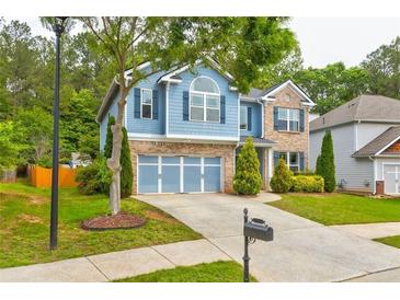 Two-story home featuring a blue facade, brick accents, manicured landscaping, and a two-car garage at 133 Parkway Dr, Fairburn, GA 30213