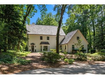 Charming two-story home with a neutral color palette, nestled amongst mature trees and lush landscaping on a sunny day at 1260 Heards Ferry Rd, Sandy Springs, GA 30328